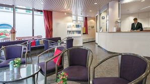 Uma área de recepção com balcão, assentos com estofamento roxo e vista para o exterior através de grandes janelas.