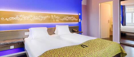 A hotel room with a large bed, a bedside table, a nightstand, and a wall with decorative lighting.