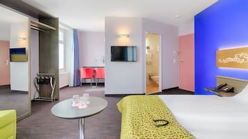 Une chambre d’hôtel comprenant un lit, une petite table avec des verres, une télévision, une salle de bain et un coin salon avec des chaises.