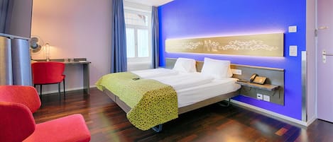 Une chambre d’hôtel avec un lit, un bureau, une chaise et un mur d’accent bleu.