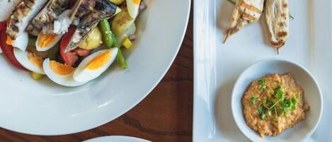 A table with three plates of food, including grilled chicken, vegetables, and a bowl of dip.
