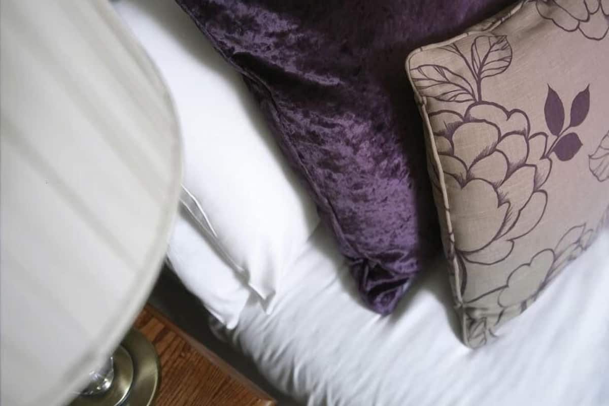 A bed with white linens, a purple pillow, and a floral-patterned pillow.
