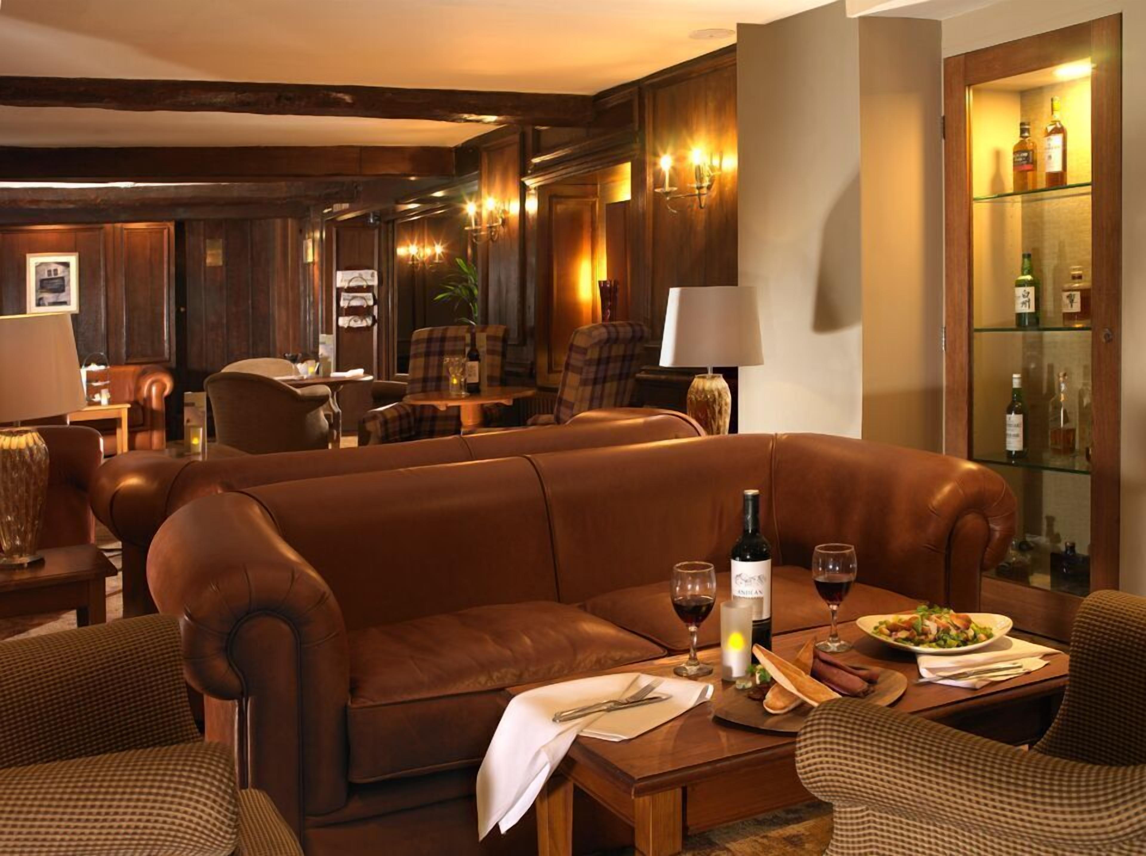 Un salón de hotel acogedor con sofás de cuero, una mesa de comedor con copas de vino y una botella, y un aparador con botellas.