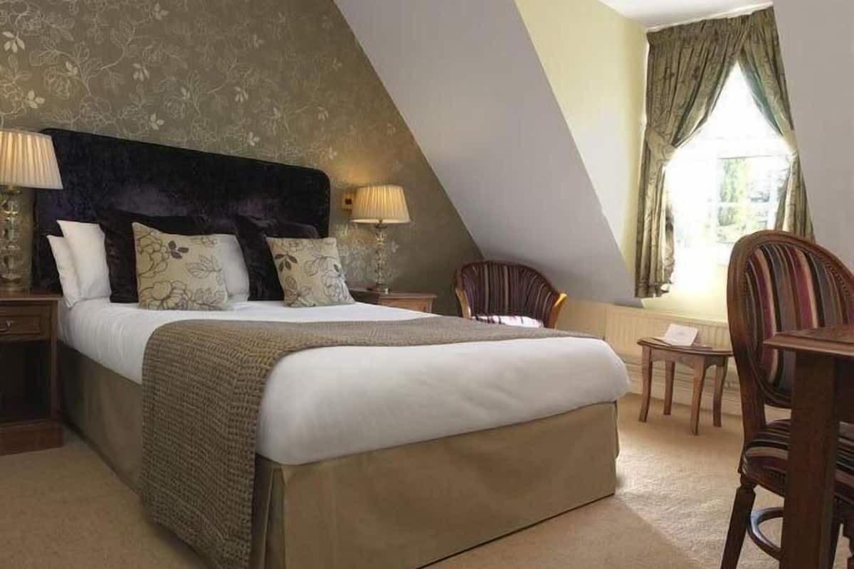 A bedroom with a large bed, two bedside tables, a chair, and a window with curtains.