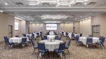 A conference room with multiple round tables, blue chairs, and a Hilton Garden Inn sign.