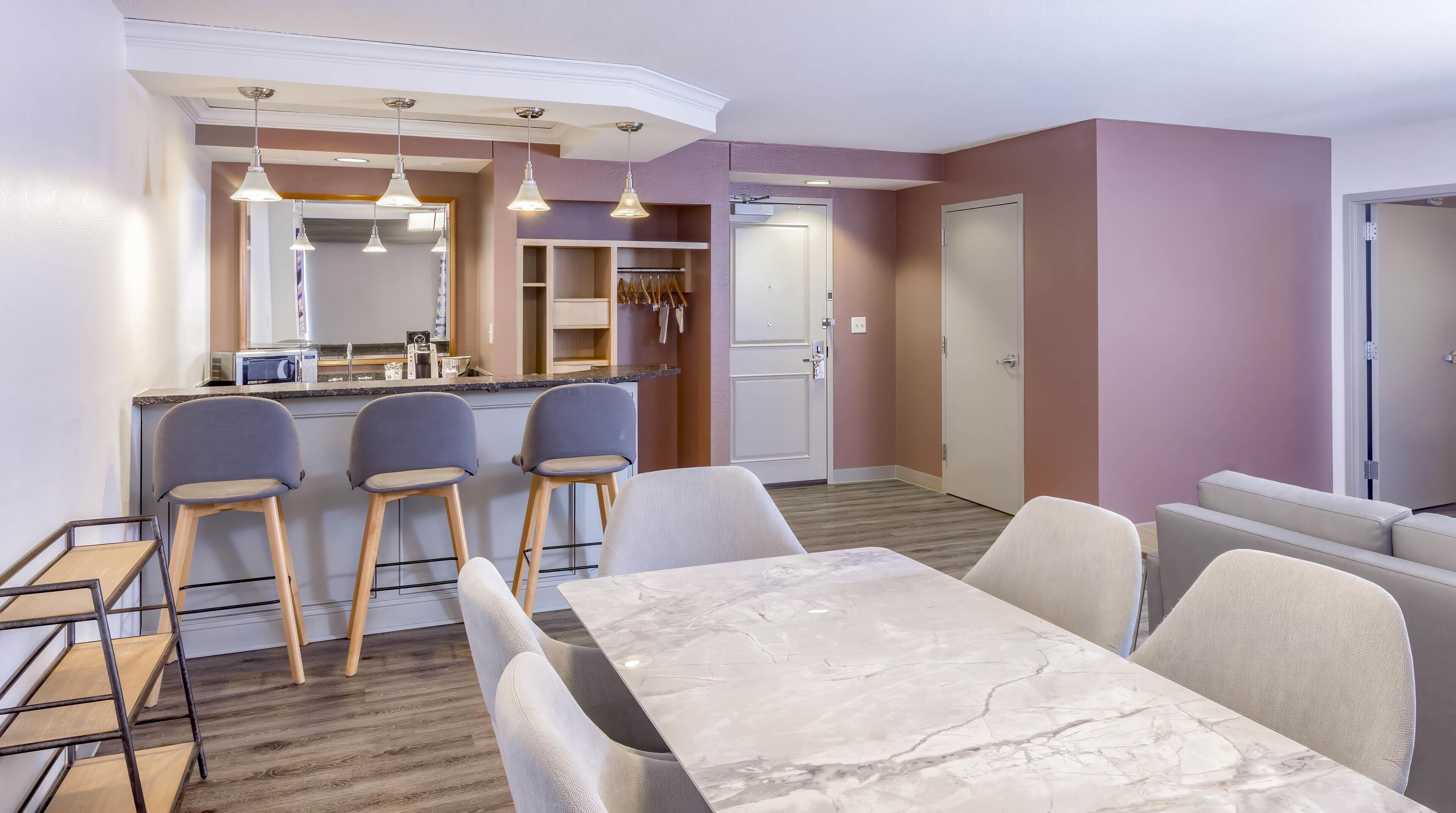 A modern kitchen with a marble countertop, bar stools, and pendant lighting.