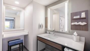 A modern bathroom with a large mirror, two sinks, a towel rack, and a bench.