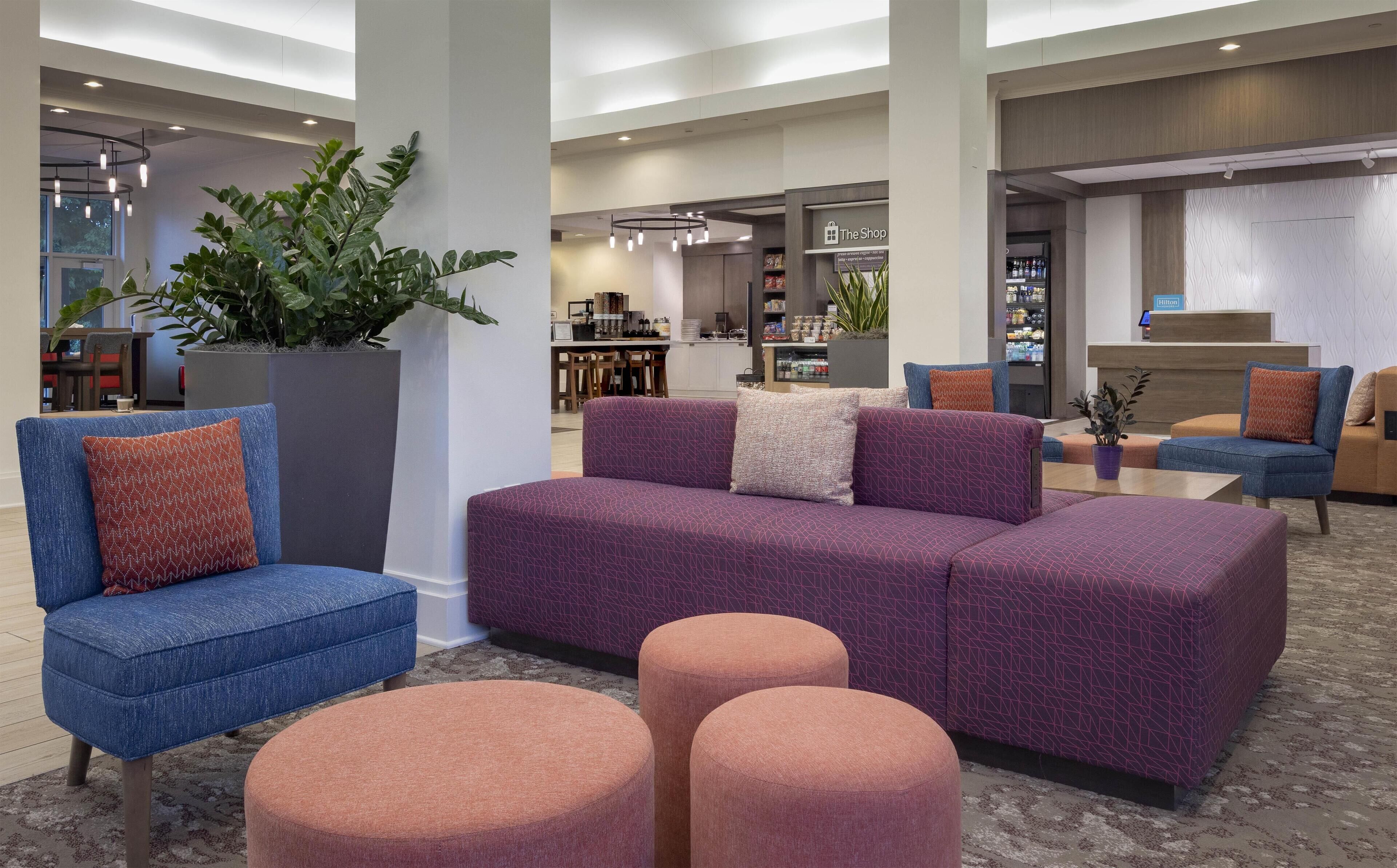 A modern lobby with a purple sofa, blue armchairs, and a large potted plant.
