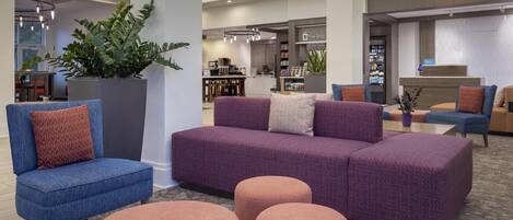 A modern lobby with a purple sofa, blue armchairs, and a large potted plant.