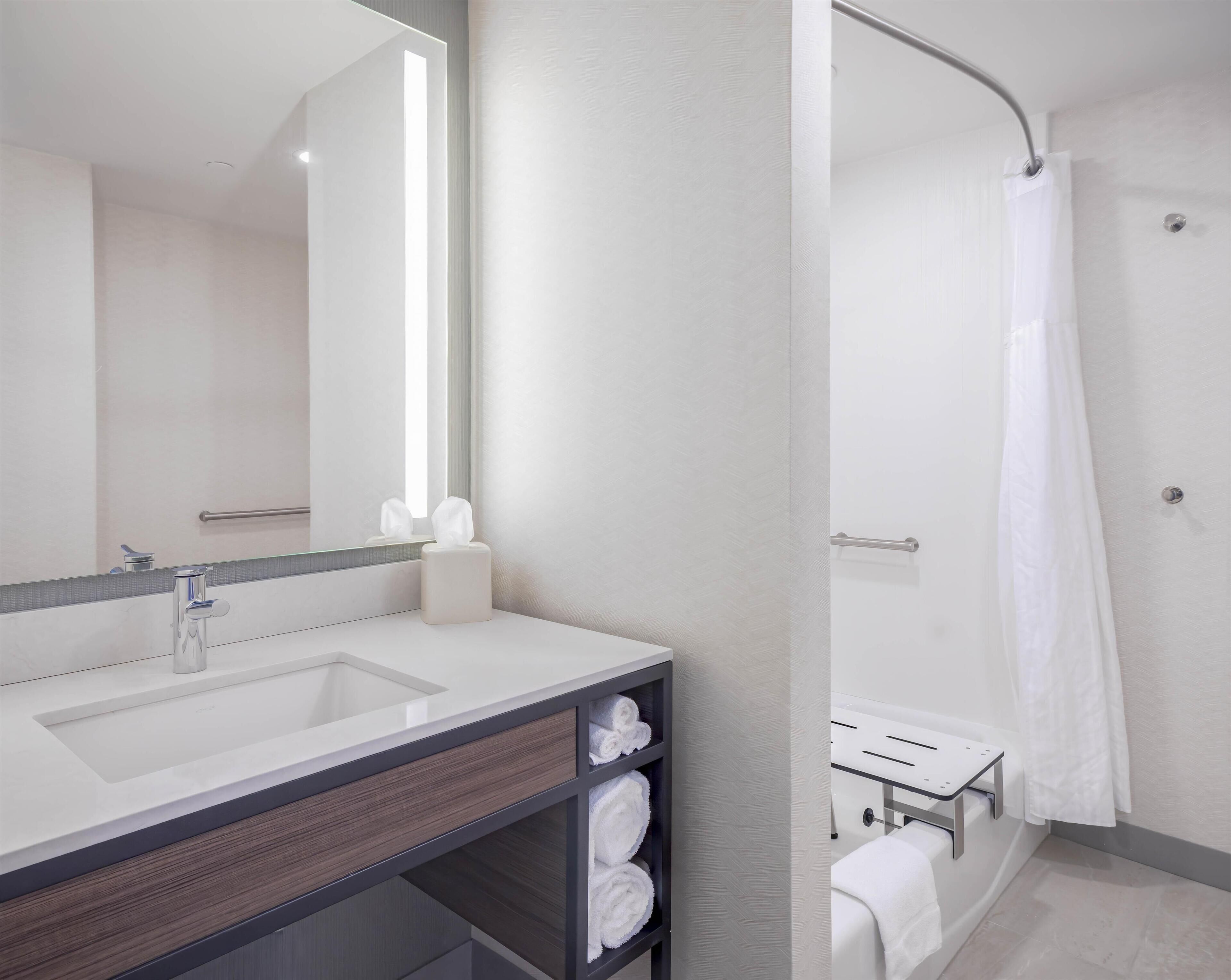 A modern bathroom with a large mirror, a sink, a towel rack, and a shower area.