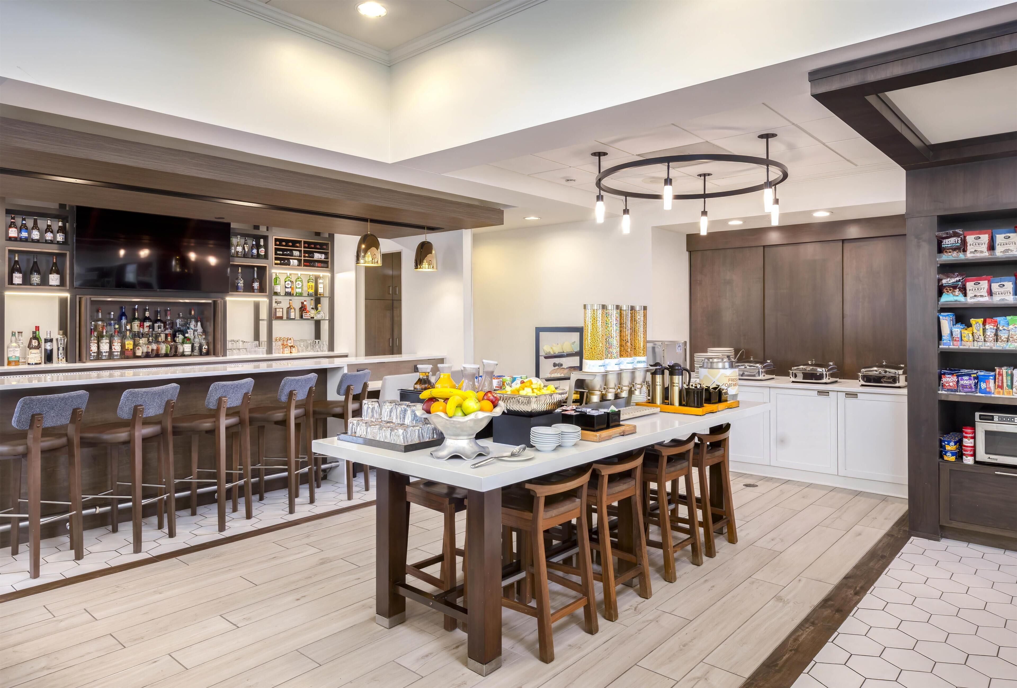 A modern kitchen with a bar area, equipped with bar stools, a fruit bowl, and various kitchen appliances.
