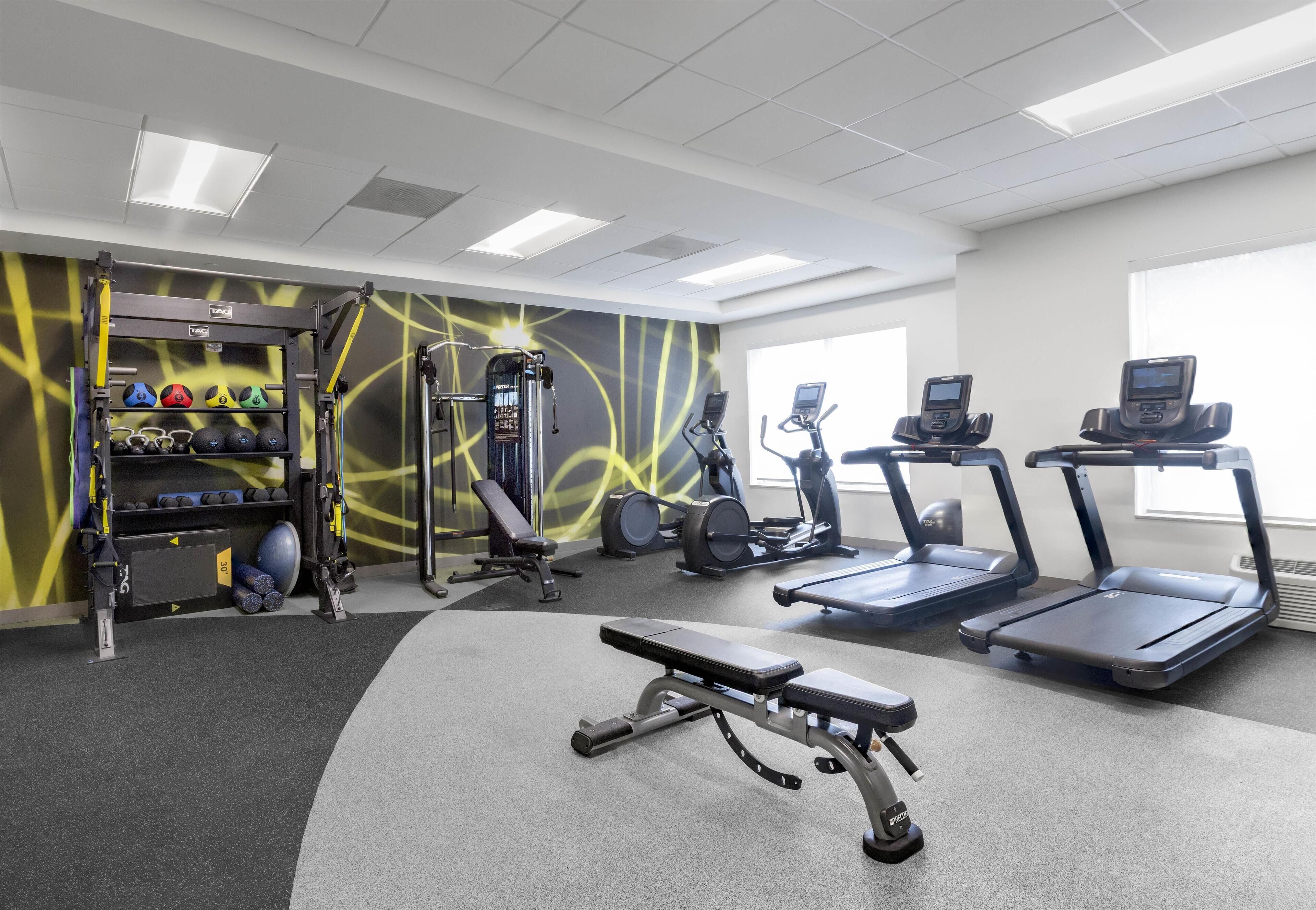 Une salle de sport équipée de tapis de course, d’un banc, d’appareils de musculation et de différents ballons d’exercice.
