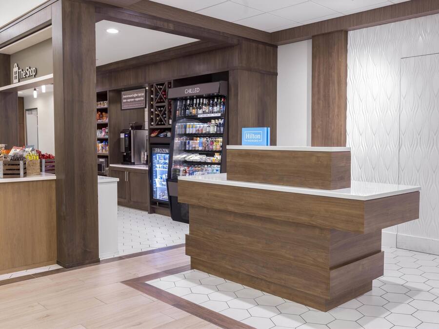 Zona de recepción de un hotel con mostrador de madera, una exhibición de bebidas frías y un minibar.