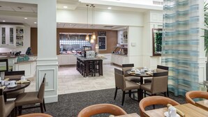 Een restaurantgedeelte in een hotel met tafels gedekt voor het ontbijt, een bar op de achtergrond en uitzicht op de keuken.