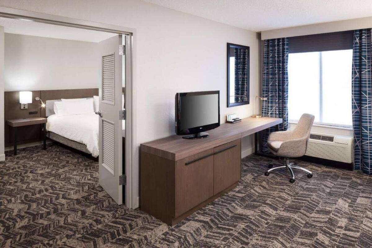 Een hotelkamer met een bed, een bureau met een televisie, een stoel en een raam met gordijnen.