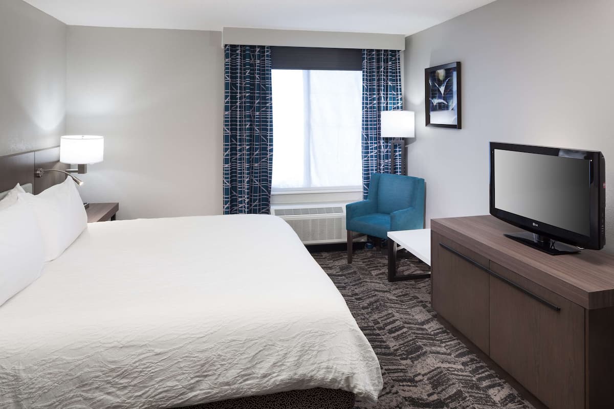 Een hotelkamer met een bed, een televisie op een houten kast, een stoel, een bureau en een raam met gordijnen.