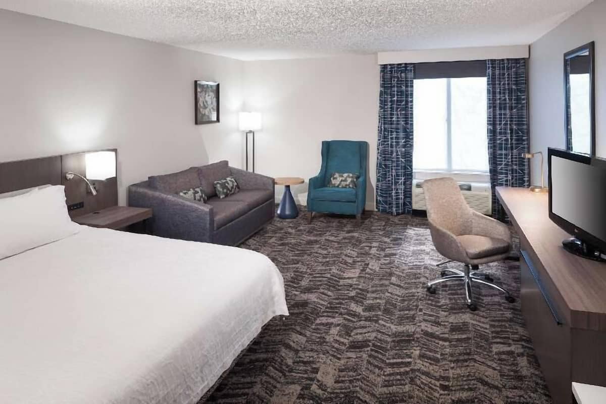 Een hotelkamer met een bed, een slaapbank, een fauteuil, een bureau met een televisie en een groot raam met gordijnen.