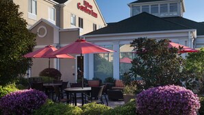 Hotelgevel met terras, rode parasols en verzorgde beplanting.