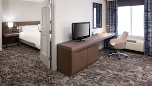 Een hotelkamer met een bed, een bureau met een computer, een stoel, een televisie en een raam met gordijnen.