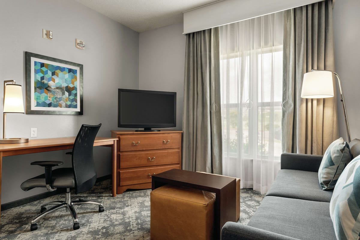 A hotel room with a desk, television, sofa, and a painting on the wall.