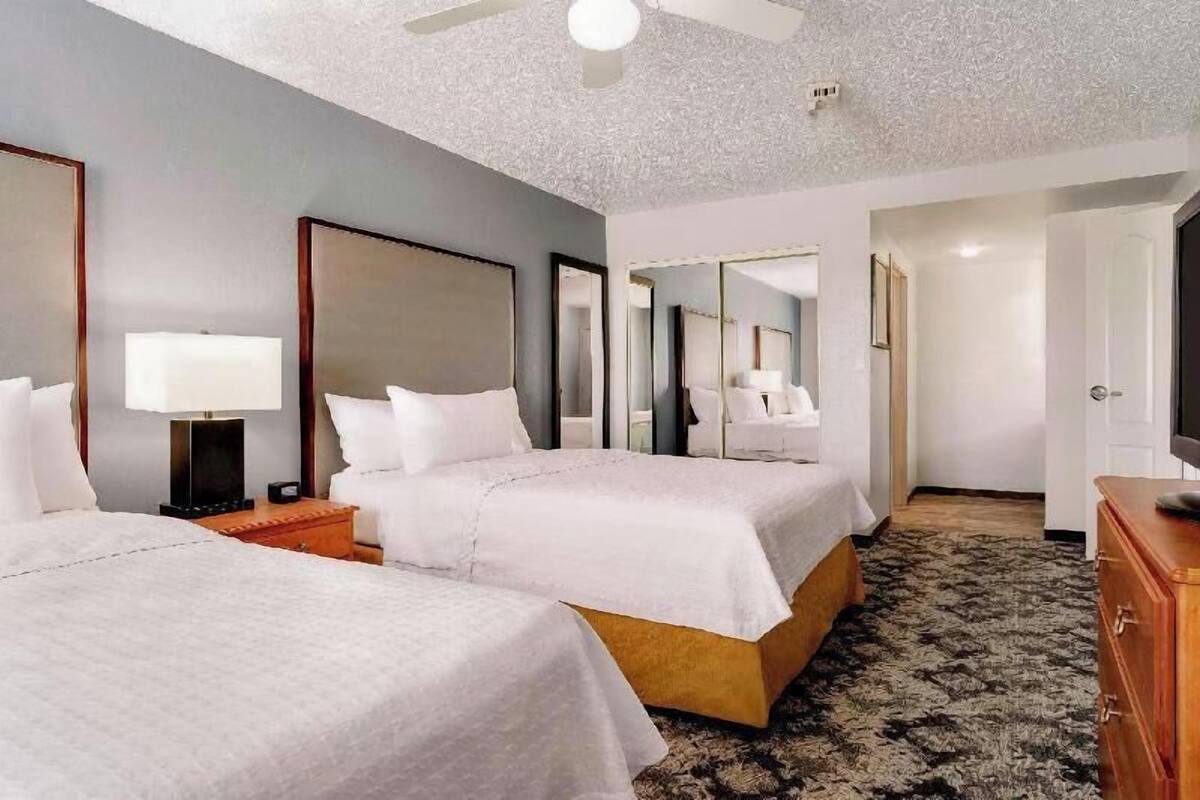 A hotel room with two beds, a ceiling fan, a large mirror, a dresser, and a carpeted floor.