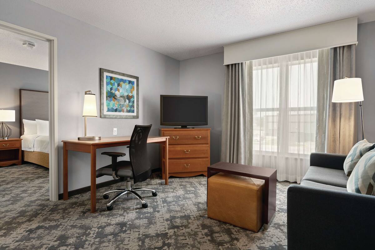A hotel room with a bed, desk, chair, TV, and a sofa.