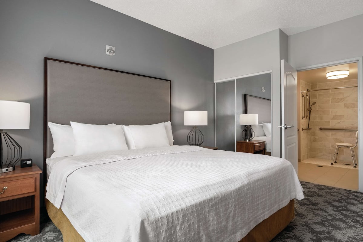 A hotel room with a large bed, bedside lamps, a nightstand, and a walk-in shower.