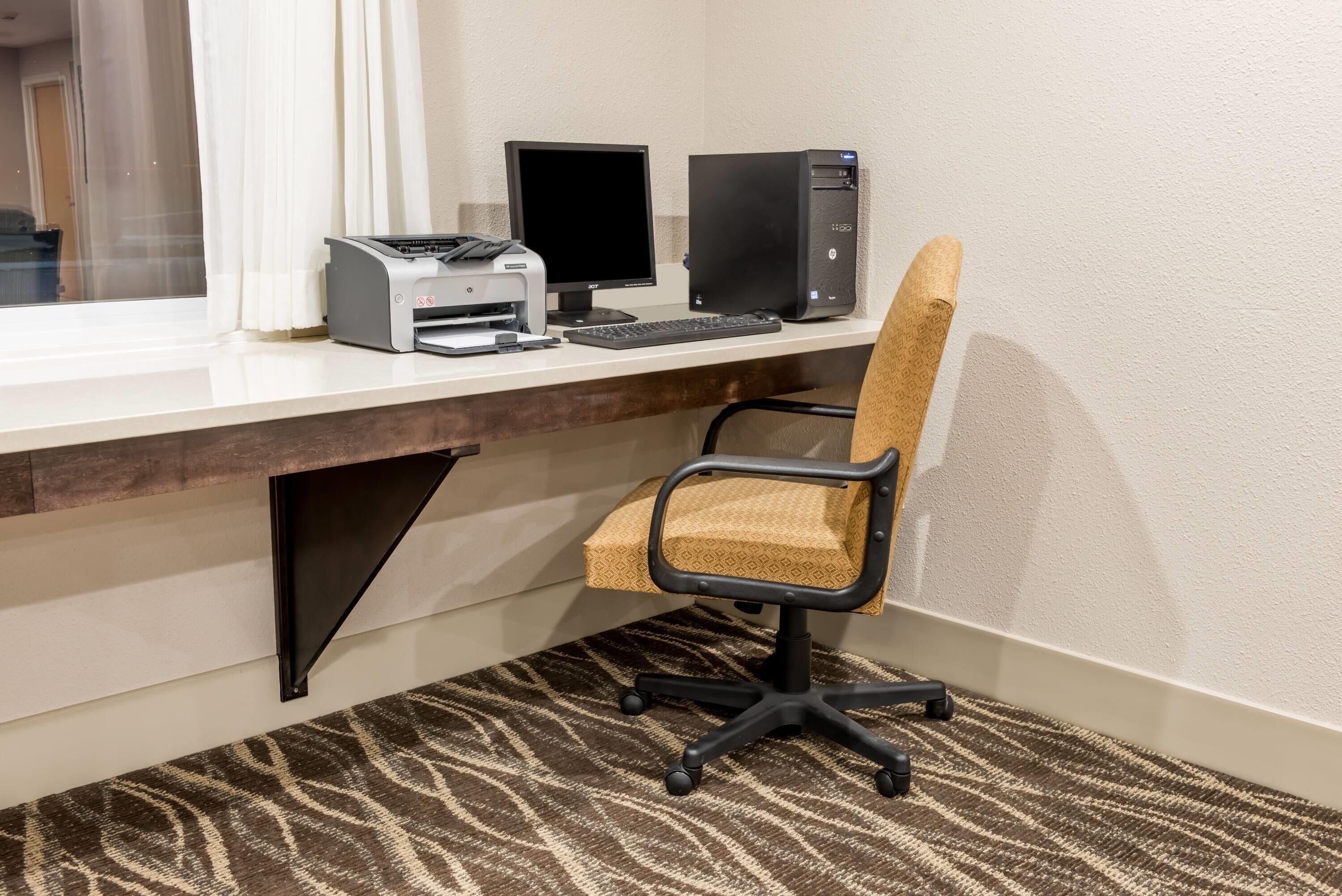 A hotel room with a desk, computer, printer, and a patterned carpet.