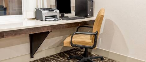 A hotel room with a desk, computer, printer, and a patterned carpet.