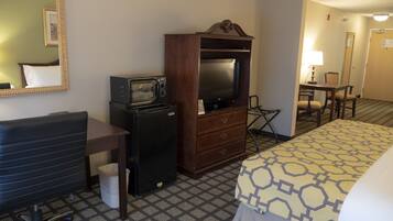 A hotel room with a bed, a desk with a computer, a television, and a minibar.