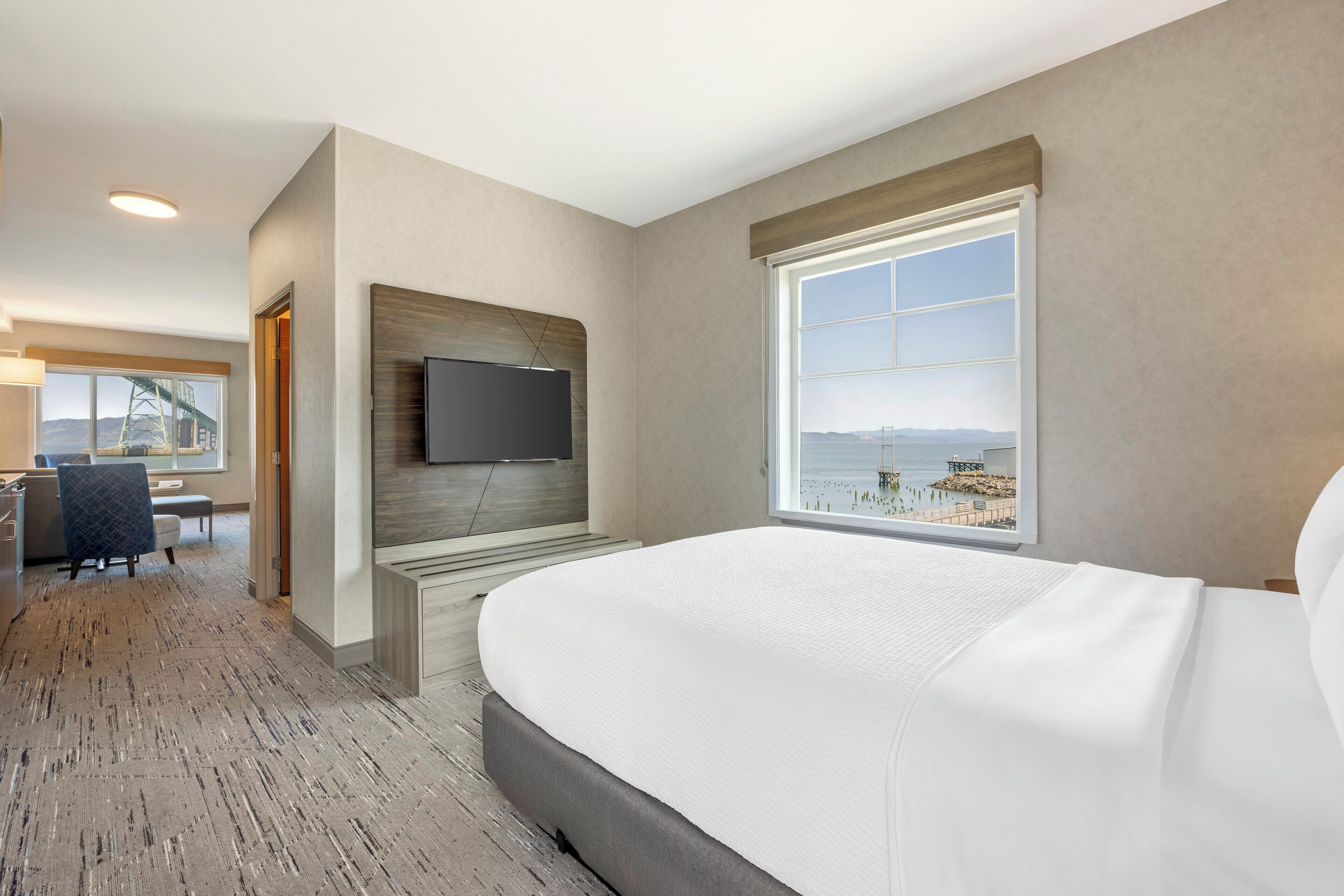 Ett hotellrum med en stor säng, en tv som är monterad på väggen och ett fönster med utsikt över en strand och berg.