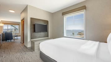 Ett hotellrum med en stor säng, en tv som är monterad på väggen och ett fönster med utsikt över en strand och berg.