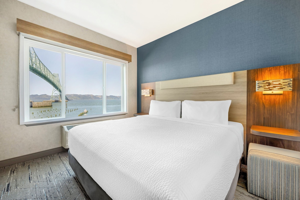 A hotel room with a large bed, a view of a bridge, and a wooden headboard.
