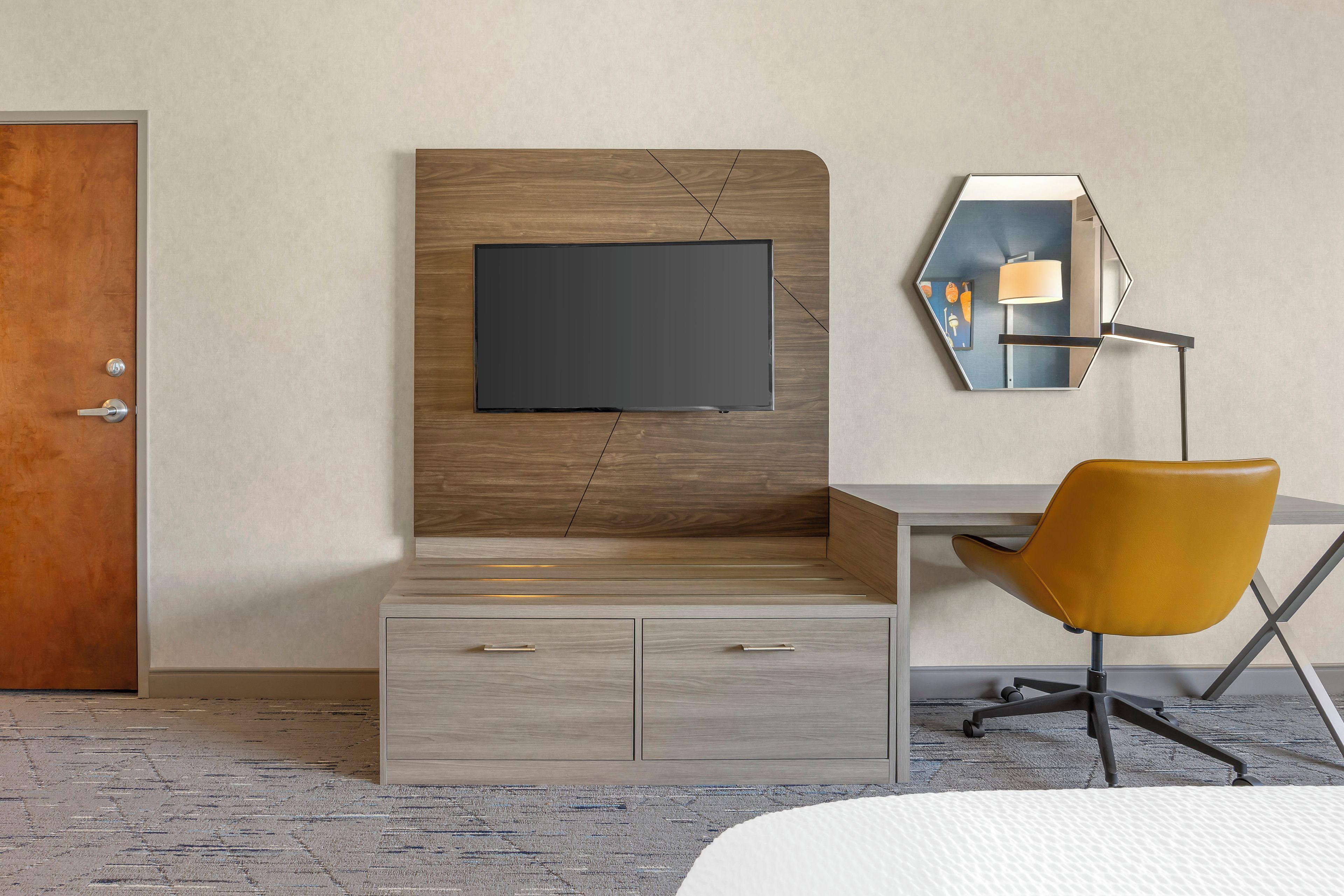 Habitació d'hotel moderna amb un panell de fusta al capçal, un televisor de pantalla plana, una taula de treball amb una cadira i un mirall fixat a la paret.