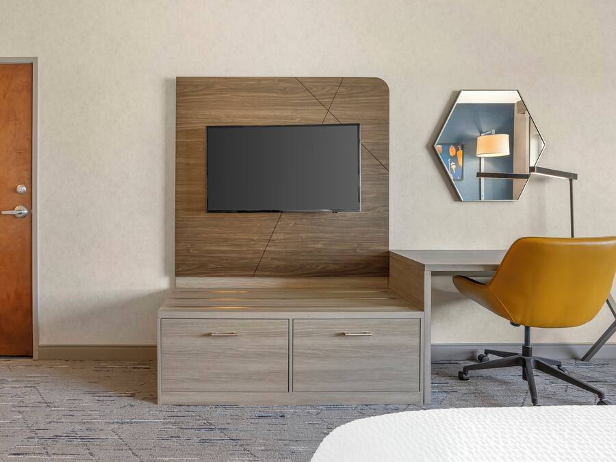 Habitació d'hotel moderna amb un panell de fusta al capçal, un televisor de pantalla plana, una taula de treball amb una cadira i un mirall fixat a la paret.