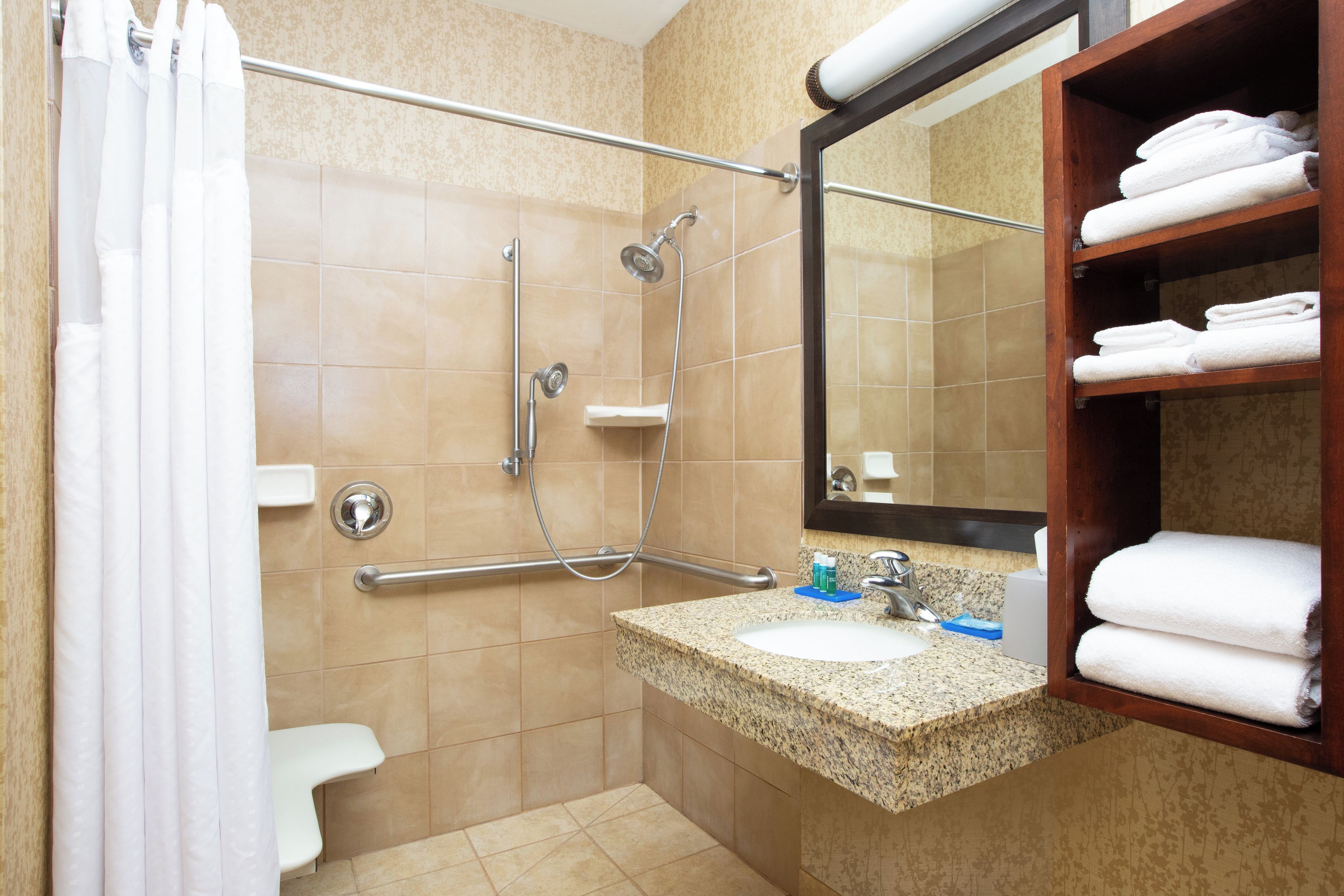 A bathroom with a shower, grab bars, a sink, and a towel rack.