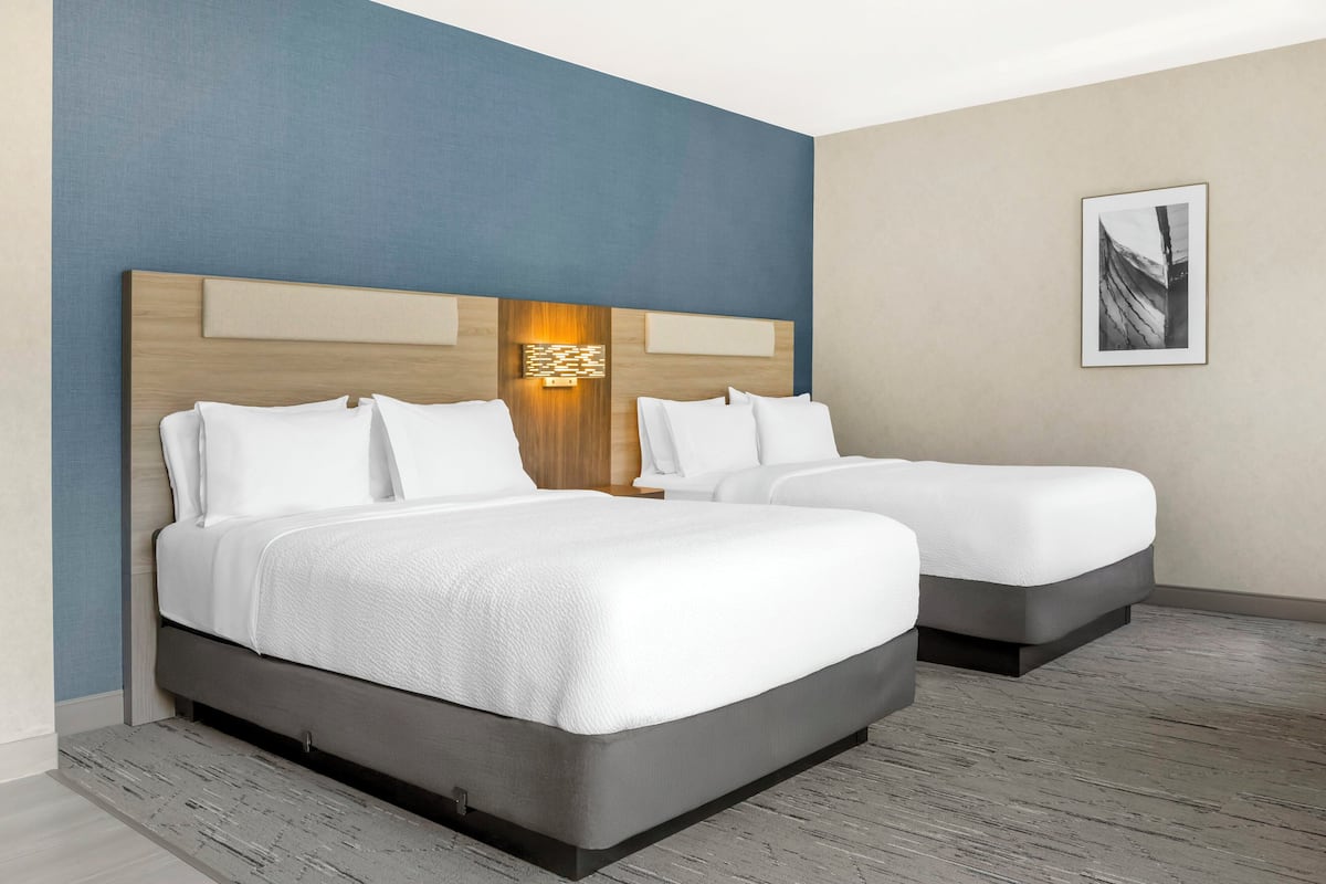 A hotel room with two beds, a wooden headboard, a wall-mounted light, and a framed picture.