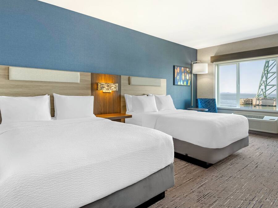 A hotel room with two beds, a large window with a view of a bridge, and a modern wall design.