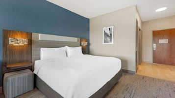A modern hotel room with a large bed, a nightstand, a wall-mounted lamp, and a framed picture on the wall.