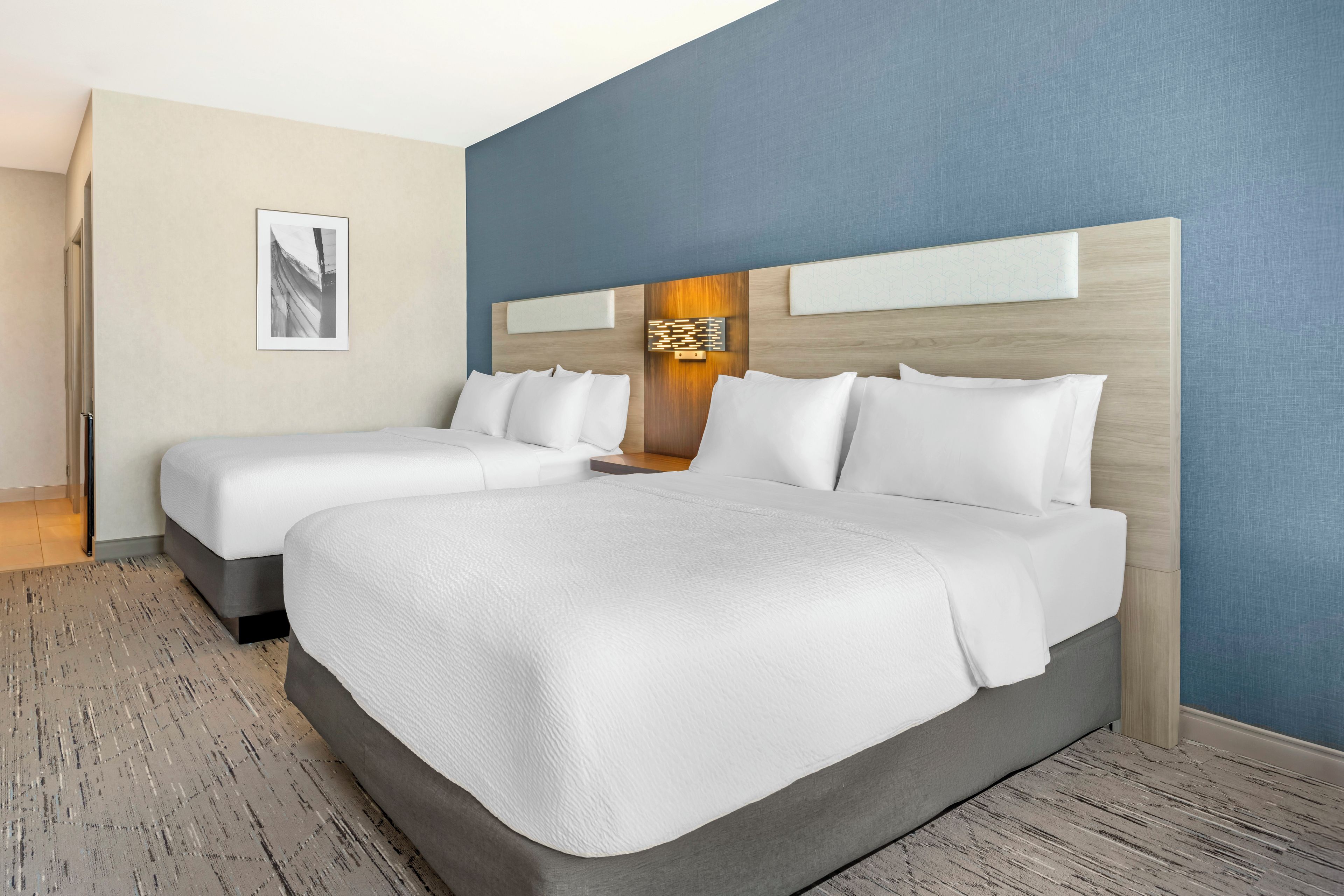 A hotel room with two beds, a large wall art piece, and a wooden headboard.
