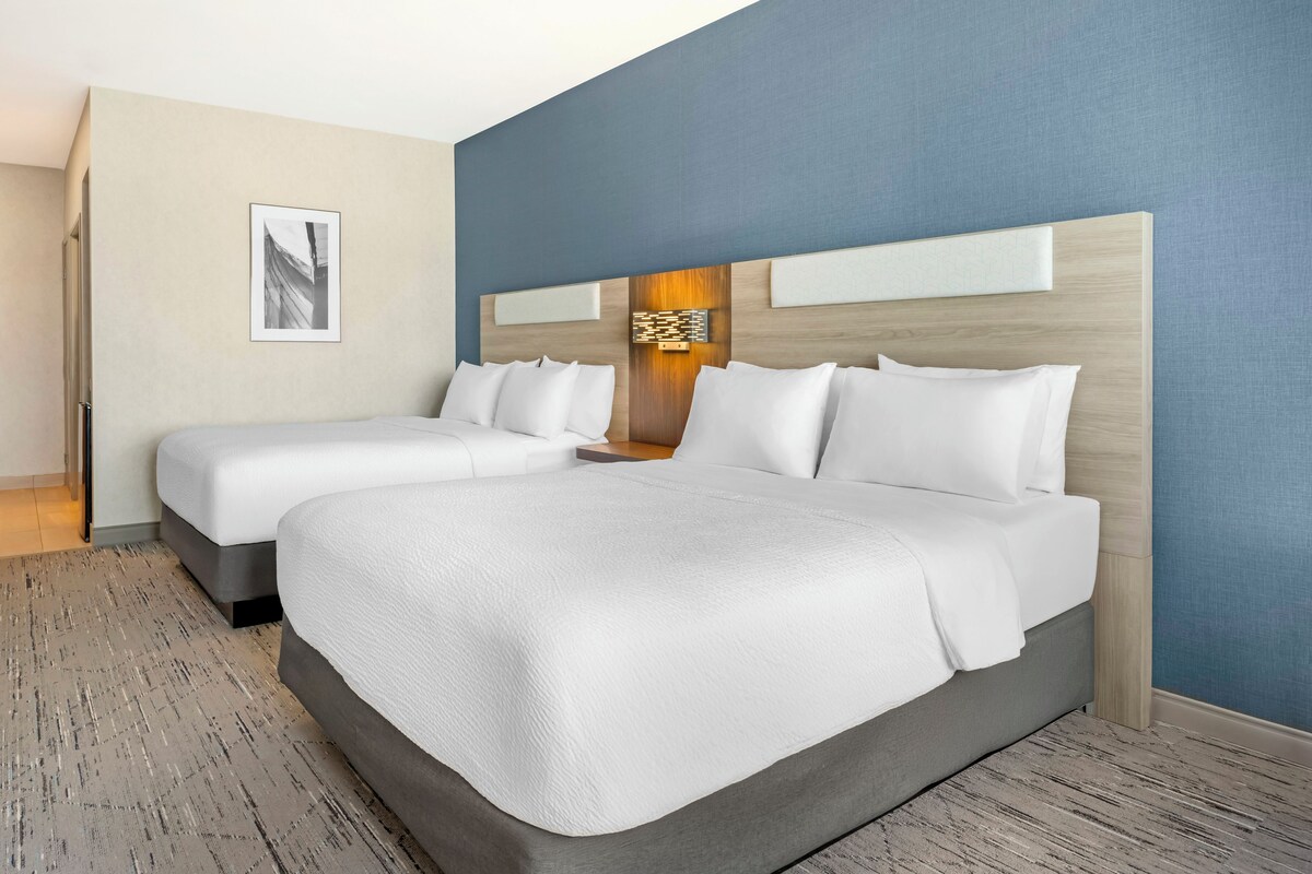 A hotel room with two beds, a large wall art piece, and a wooden headboard.