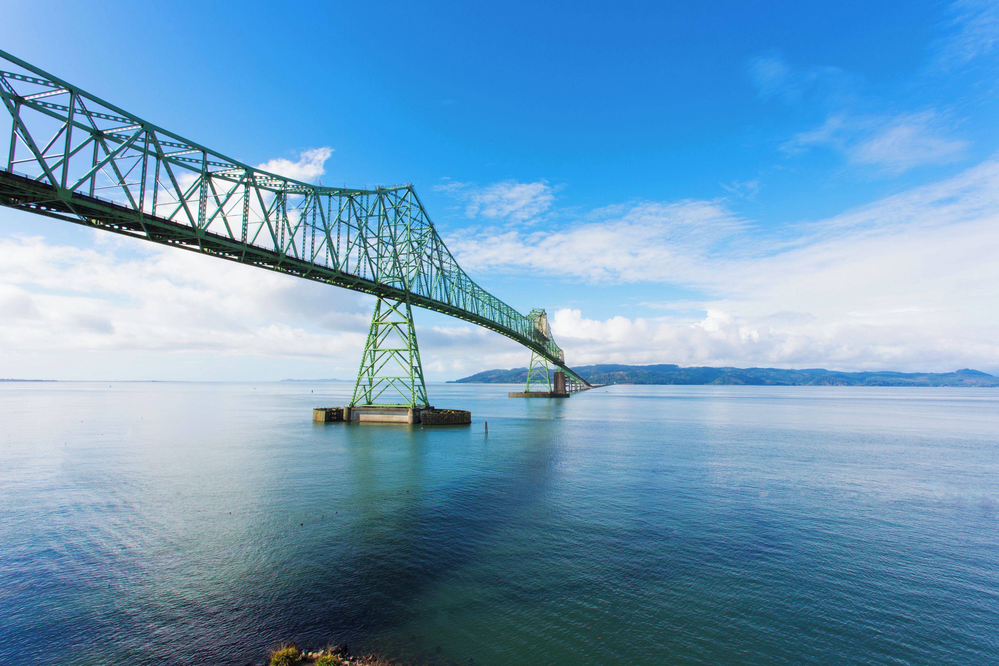 A large green steel bridge spanning a calm body of water with a clear sky above.