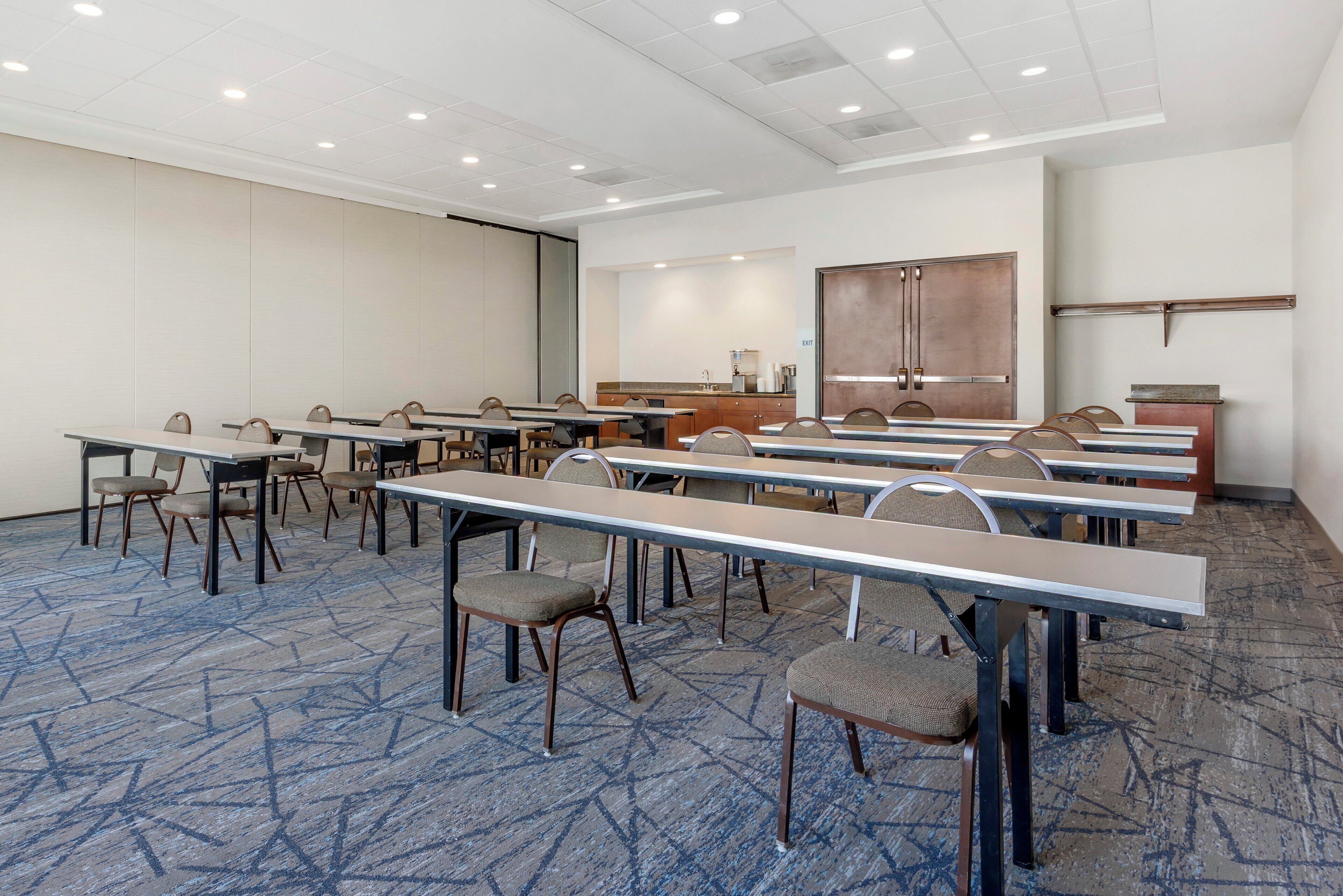 A conference room with multiple tables and chairs, a projector screen, a kitchenette, and a large cabinet.