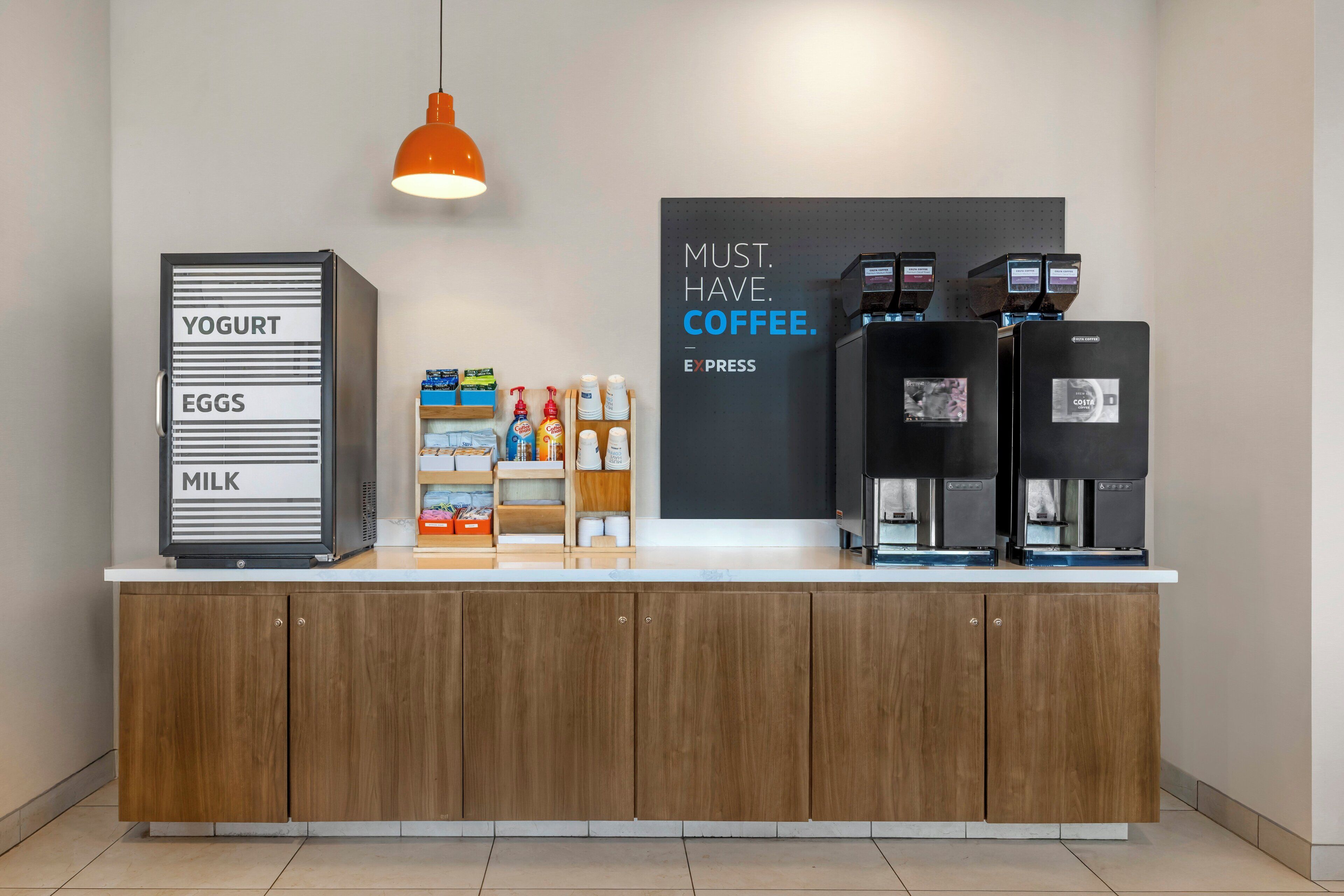 A counter with a coffee station, labeled with 'YOGURT,' 'EGGS,' and 'MILK.' There are coffee machines and a sign that says 'MUST. HAVE. COFFEE.'