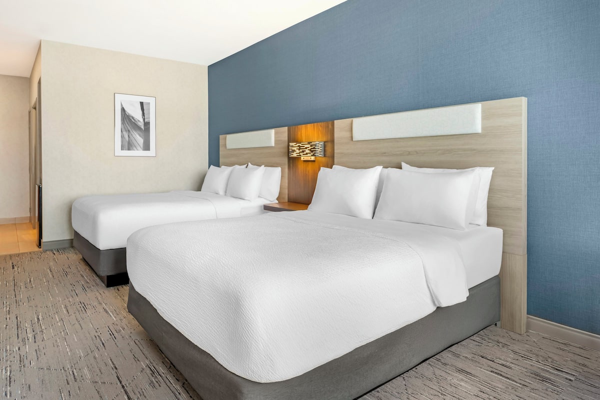A hotel room with two beds, a large wall art piece, and a wooden headboard.