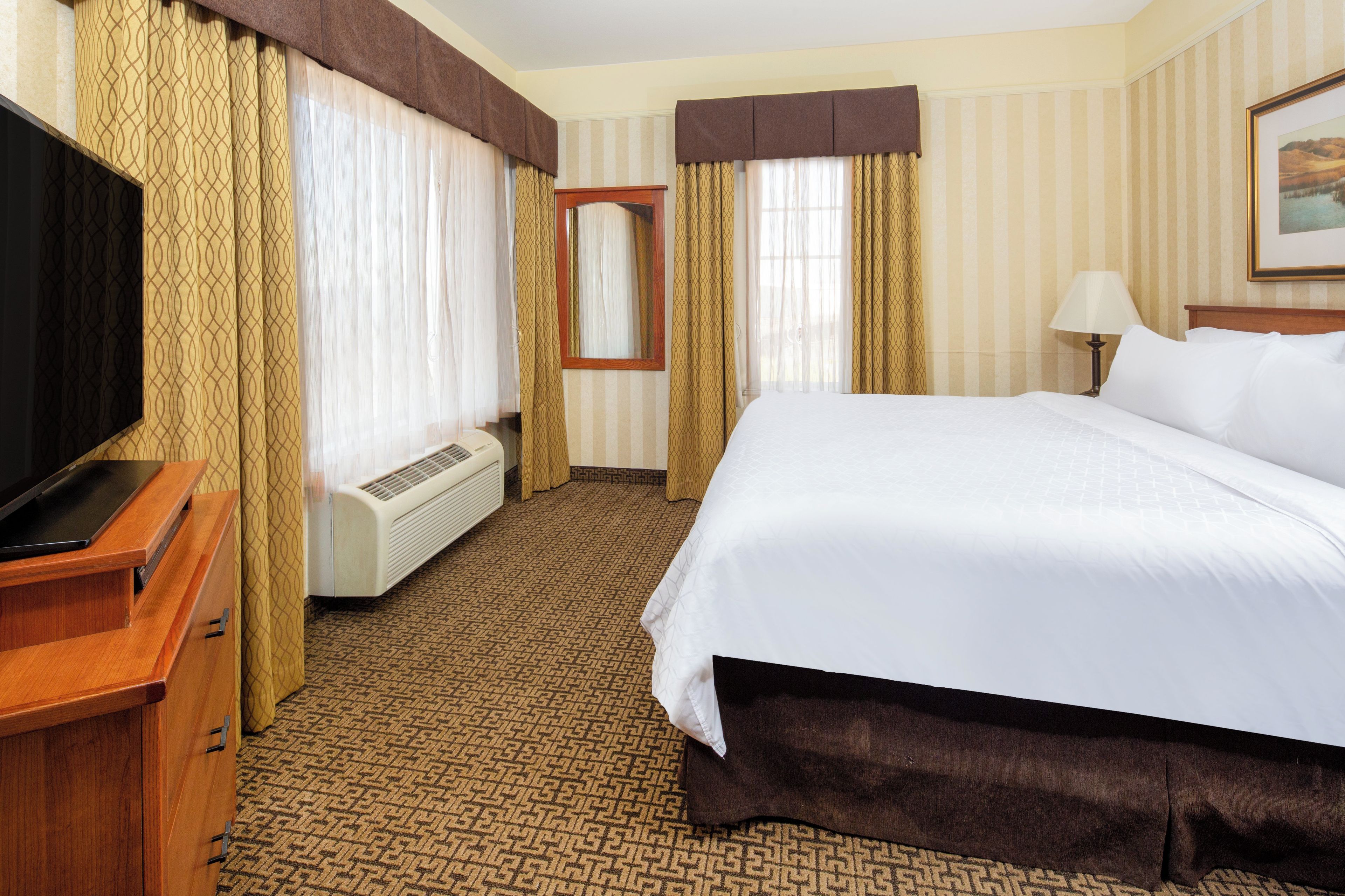 A hotel room with a bed, a TV, a desk, and a window with curtains.