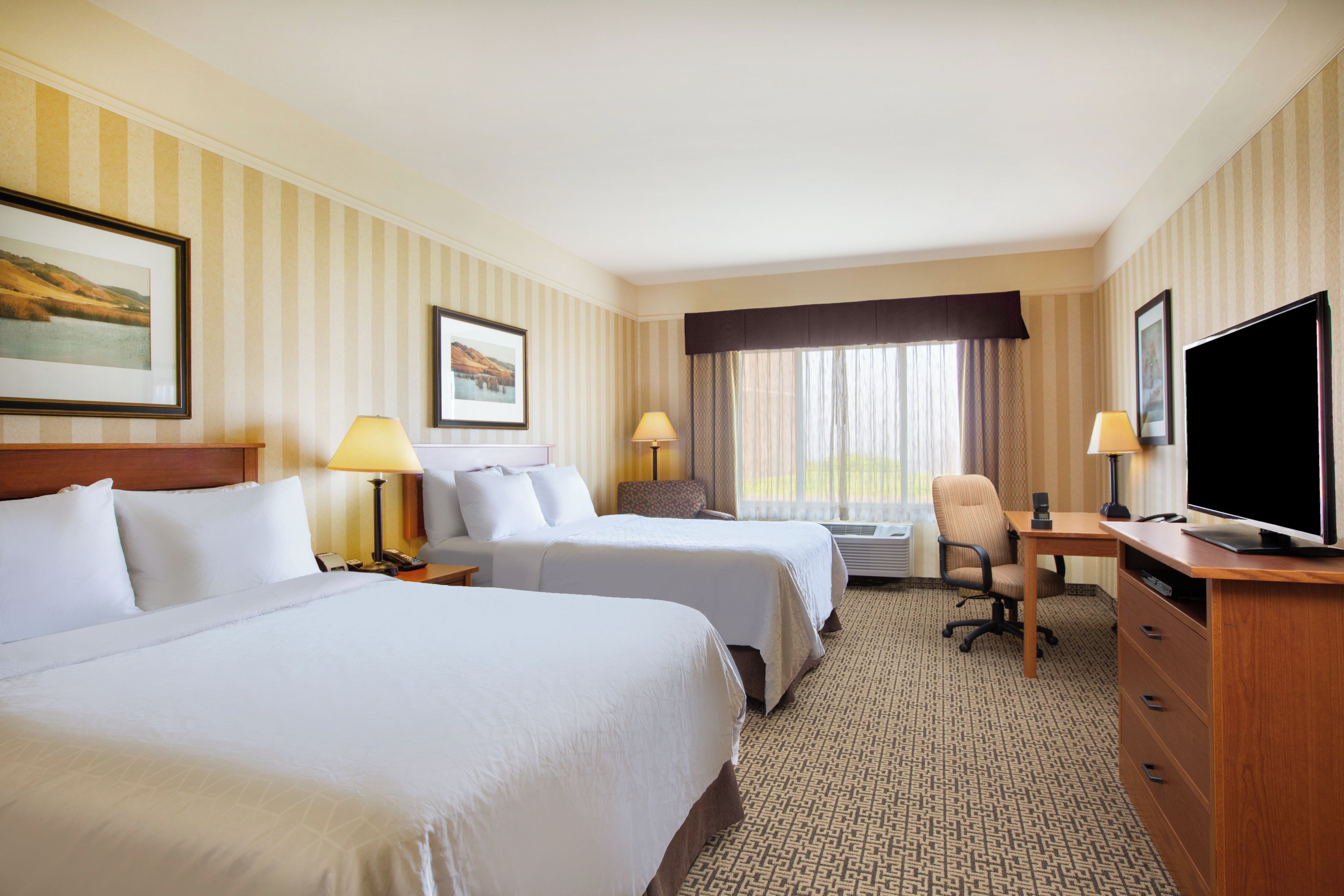 A hotel room with two beds, a desk with a television, and a chair.