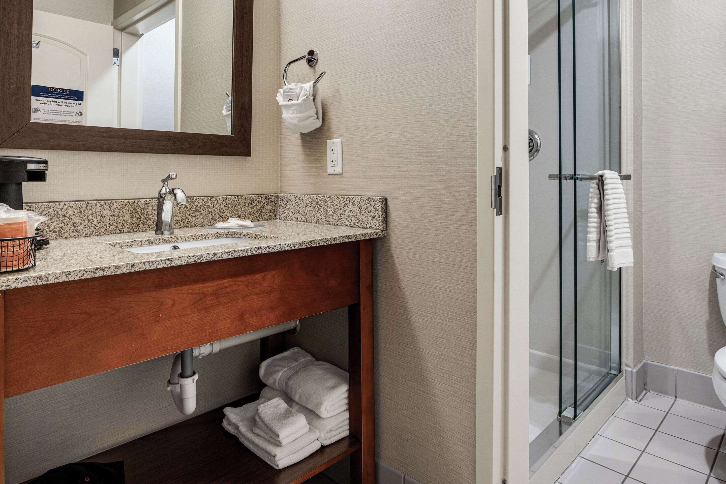Une salle de bain avec un lavabo sur un plan de travail en granit, un meuble-lavabo en bois, une cabine de douche en verre et des toilettes blanches.