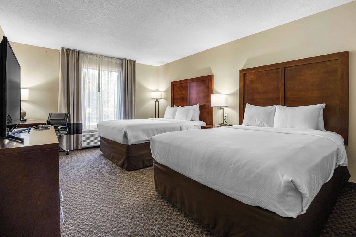 Ein Hotelzimmer mit zwei Betten, einem Schreibtisch, einem Stuhl und einem Fernseher.