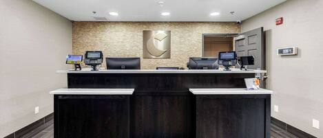 Un área de recepción con un mostrador de madera oscura, dos monitores de computadora y un logotipo montado en la pared.